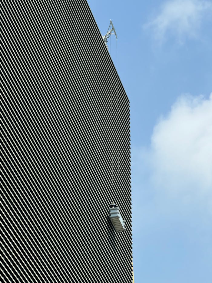 About A window cleaner ascends a tall building on a clear day with blue skies.